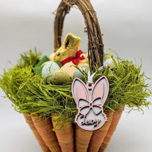 Load image into Gallery viewer, Pictured is an easter basket shaped like vertically stacked carrots, with raffia greens and a grapevine handle. The basket contains pastel, spotted eggs and a gold-wrapped chocolate rabbit. On the basket hangs a personalized, layered wood tag cut in the shape of a rabbit's head. Two ears protrude upward, there is a bow across the forhead, and the "face" of the rabbit incorporates the name "Lucy" into the cut design in a script font.